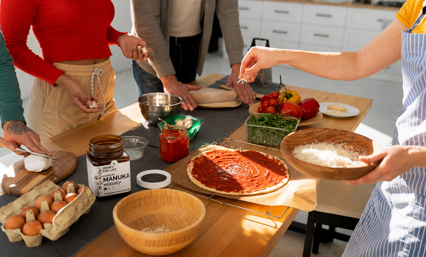 Friends making homemade pizza in a bright kitchen using Manuka honey as a natural sweetener ingredient