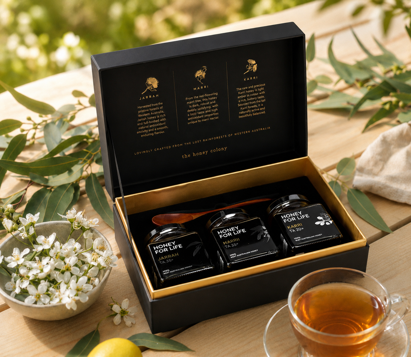 Honey jar gift box set on top of the table beside with white flowers on a bowl and a cup of tea.