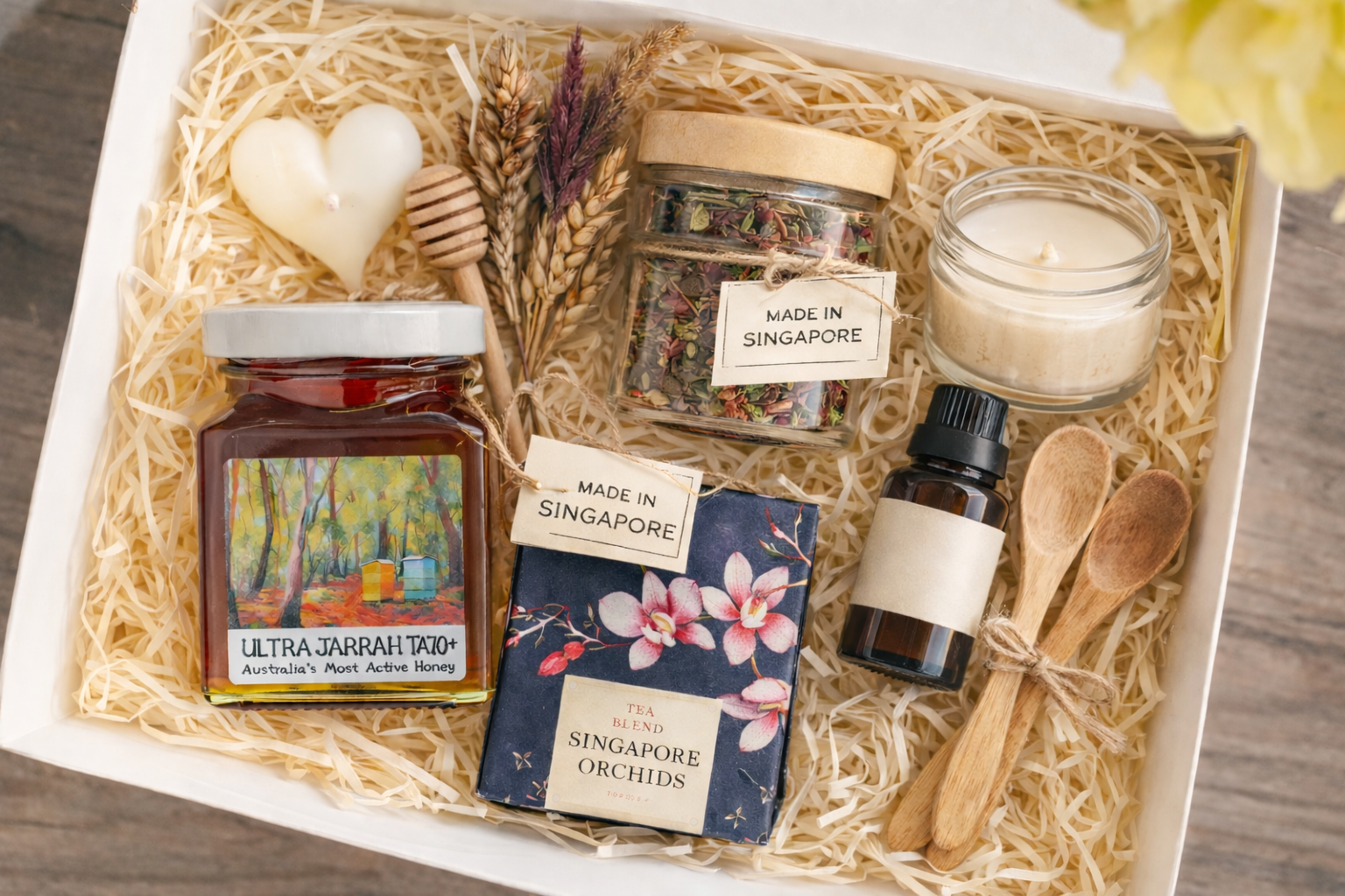 Premium gift box featuring honey jar, tea blend, heart-shaped candle, essential oil, wooden spoons, and dried flowers on shredded paper.