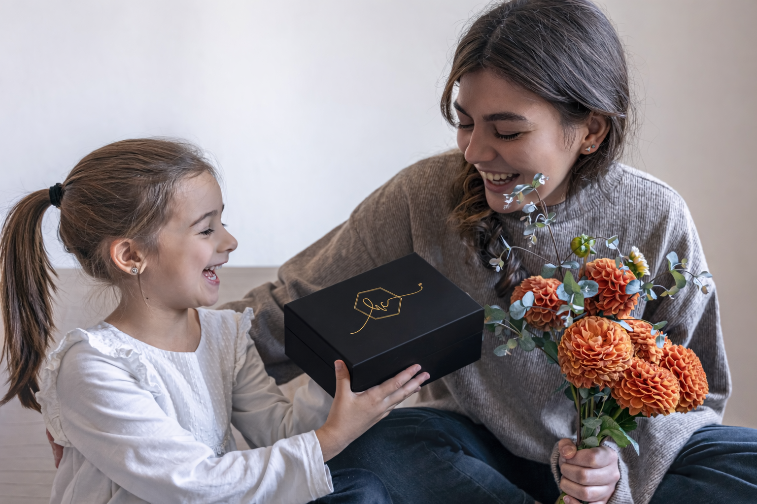 Daughter giving her mother a black luxury gift box with flowers, smiling together during a Mother’s Day moment