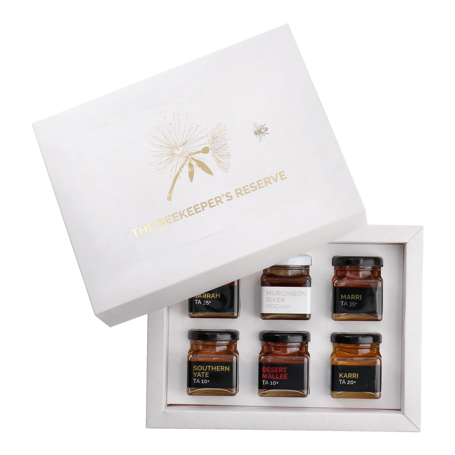 A set of six small, clear jars of honey arranged in a white rectangular box, with a gold bee design on the box lid. The set is labeled as 'Beekeeper's Reserve' and each jar has a different variety name.