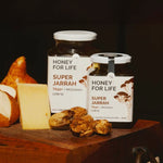 Two jars of 'Honey for Life Super Jarrah' on a wooden surface with fruits and nuts.
