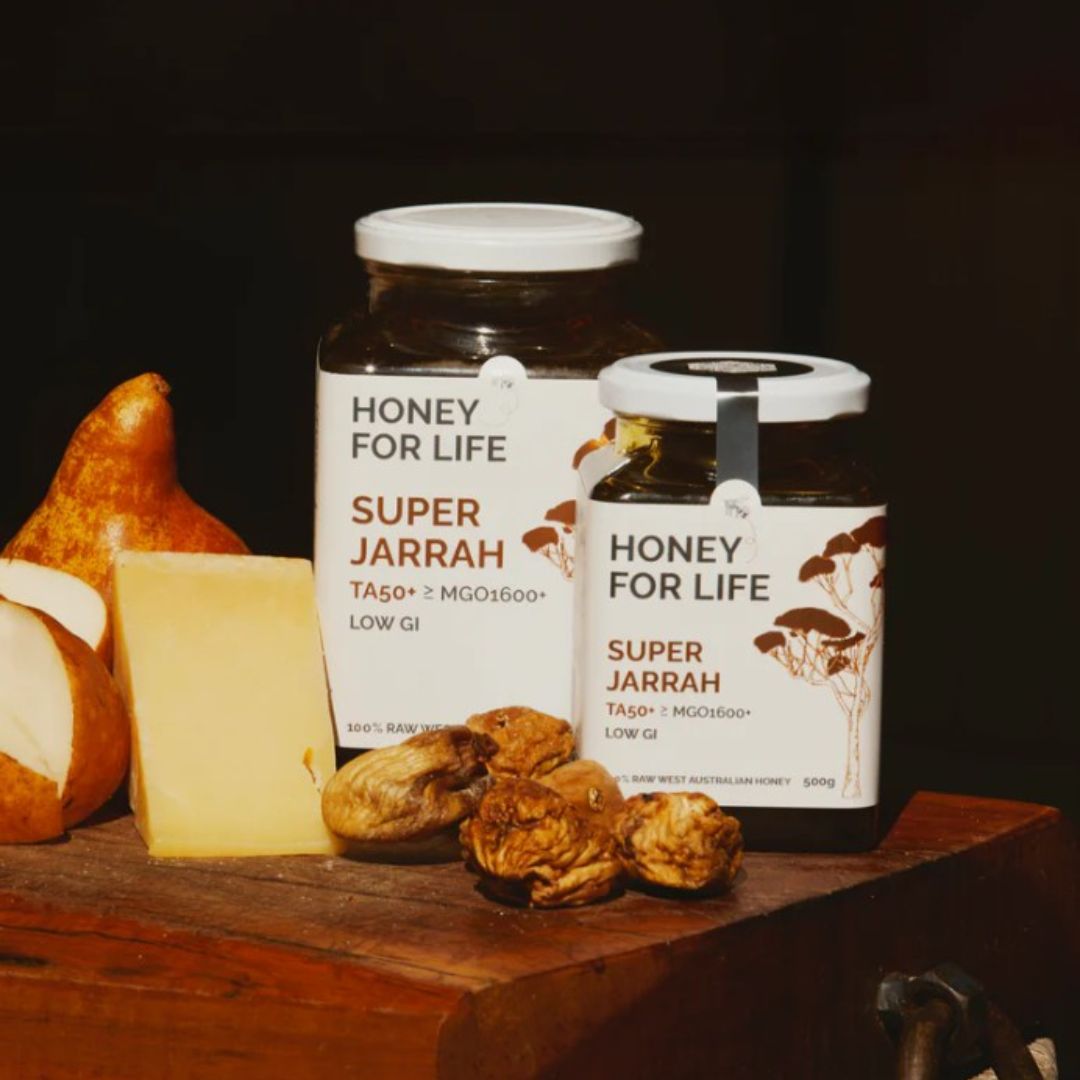 Two jars of 'Honey for Life Super Jarrah' on a wooden surface with fruits and nuts.