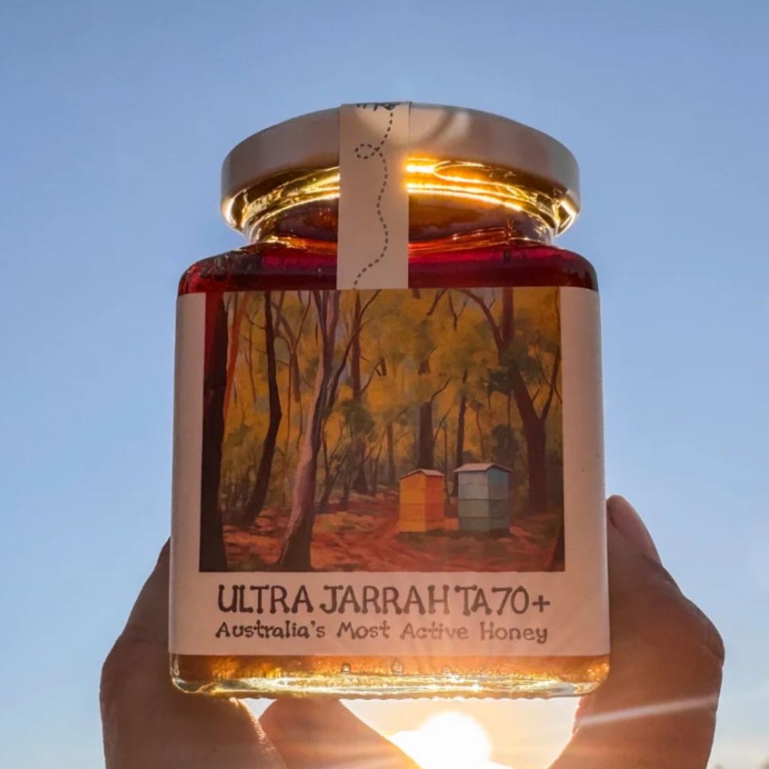 Jar of Ultra Jarrah TA70+ honey with a scenic label against a clear blue sky.