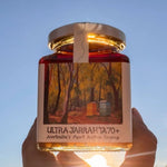 Jar of Ultra Jarrah TA70+ honey with a scenic label against a clear blue sky.
