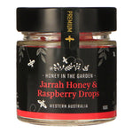 A jar of Jarrah Honey & Raspberry Drops with a label that includes images of honeycombs, raspberries, and a bee. The text on the label reads 'Honey in the Garden' and 'Jarrah Honey & Raspberry Drops, Western Australia 150g'.